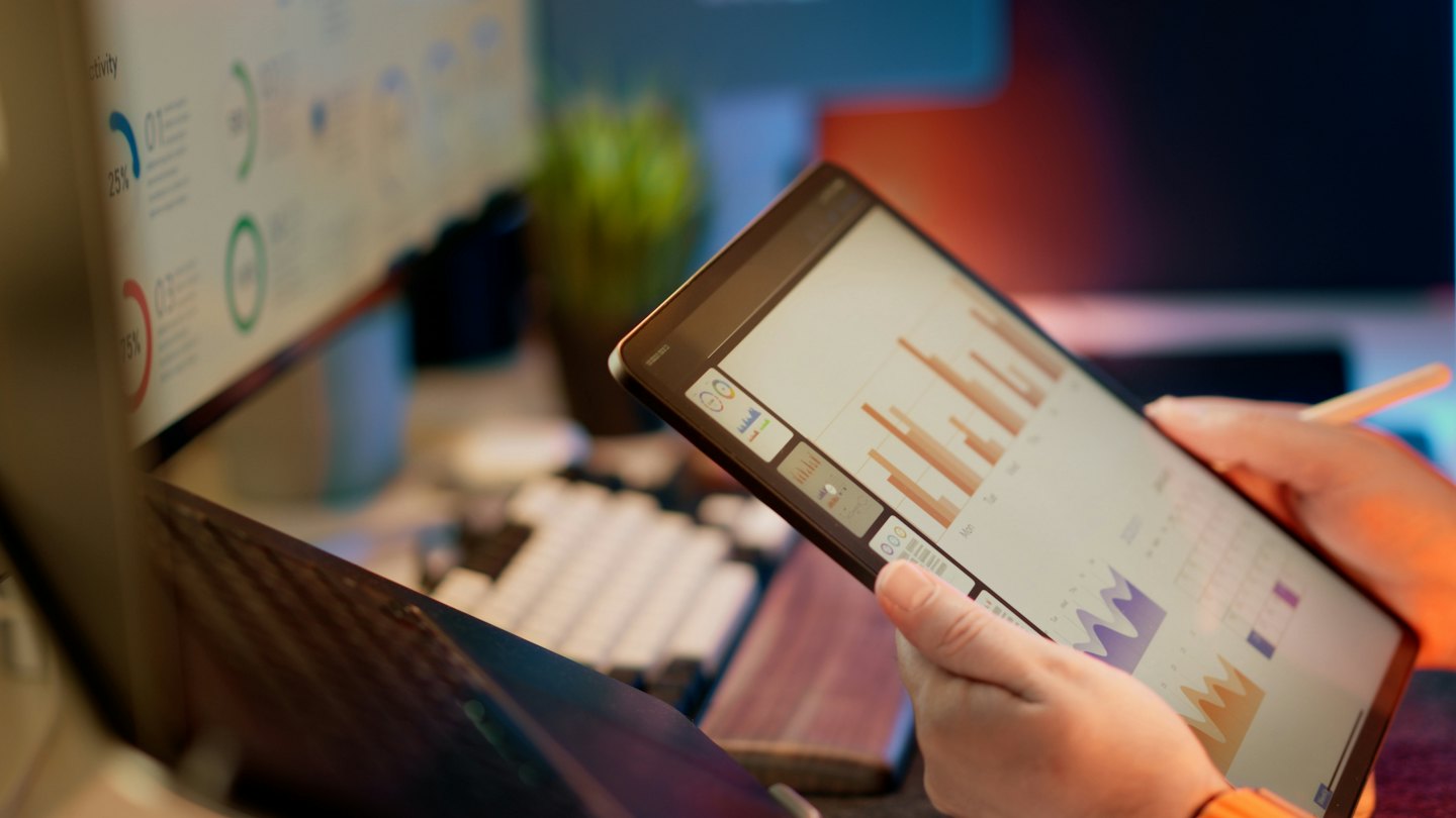 Person analysiert Geschäftsdiagramme auf einem Tablet am Schreibtisch.